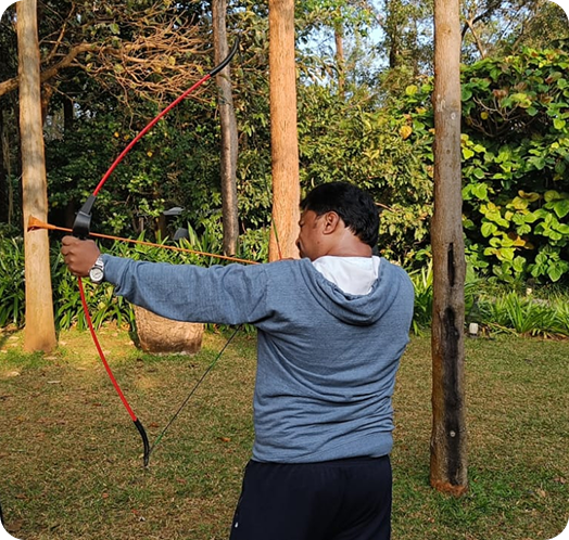 Employee practicing archery outdoors in a wooded area while aiming a bow and arrow at a target.