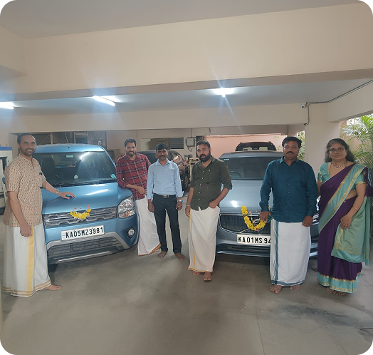 Employees posing beside two newly inaugurated company vehicles decorated with flowers in a parking area.