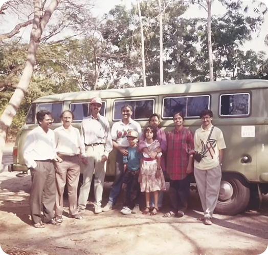 Company team members and their families standing together in front of a vintage van during an outdoor gathering.