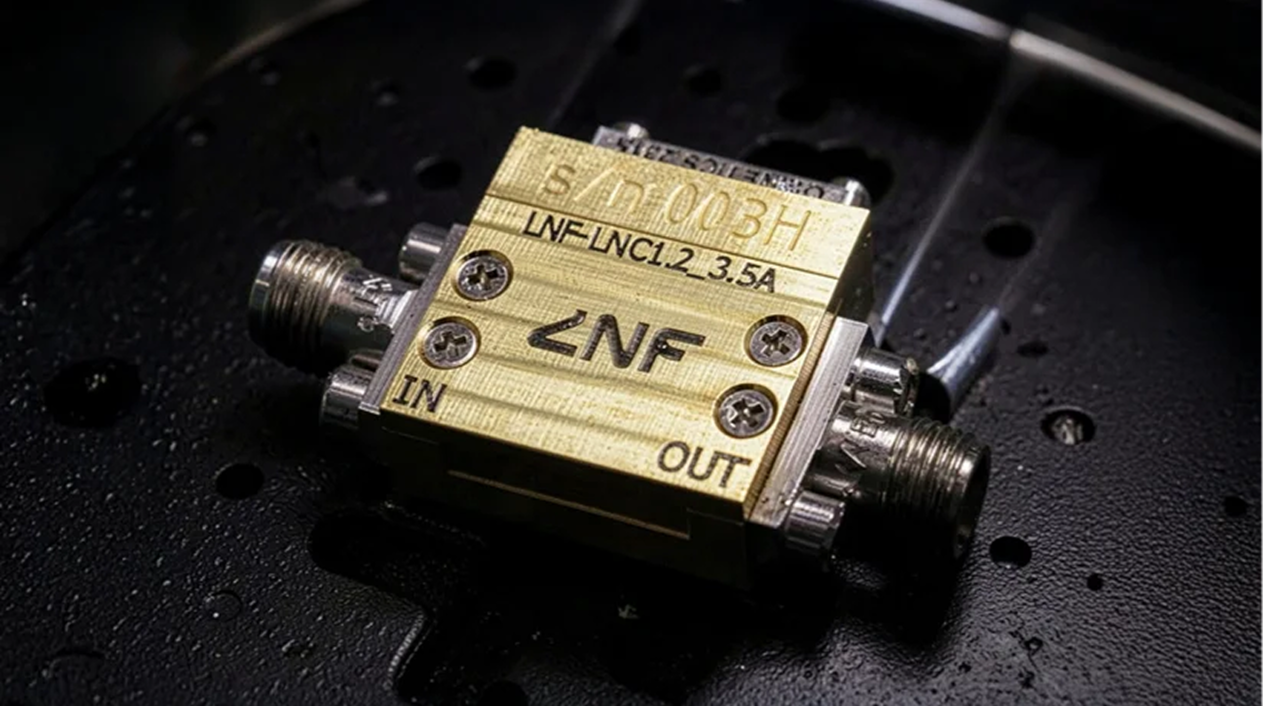 Close-up of a cryogenic low noise amplifier with RF connectors labeled IN and OUT.